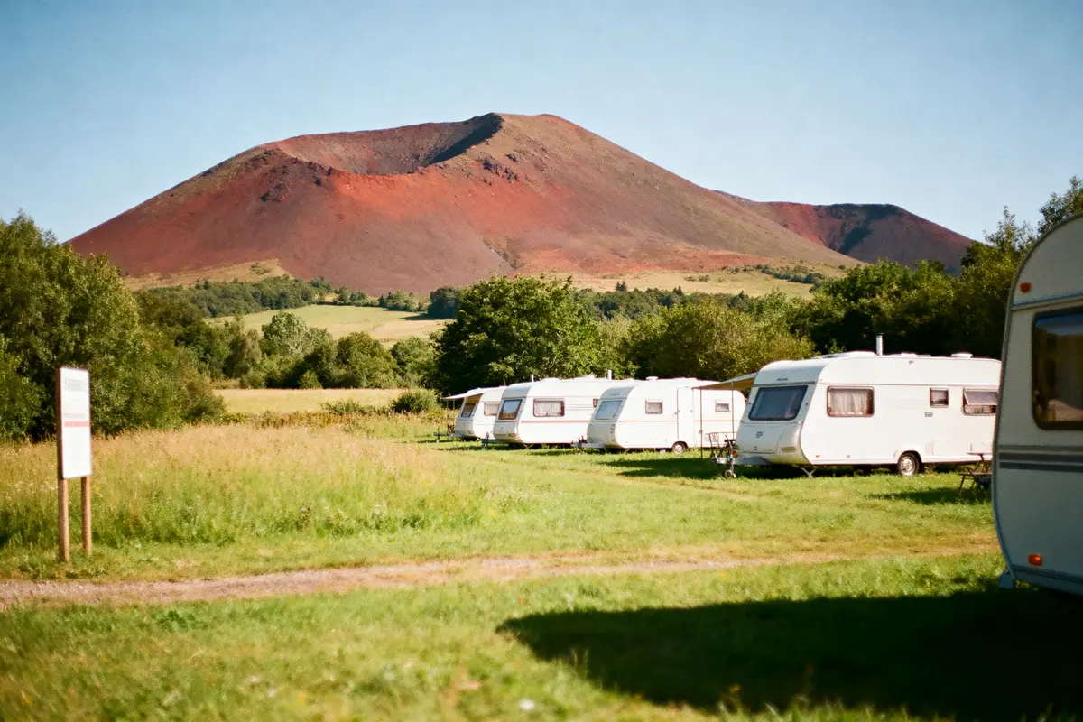 Caravanes blanches alignées sur pelouse verte, avec volcan en arrière-plan sous ciel bleu clair.