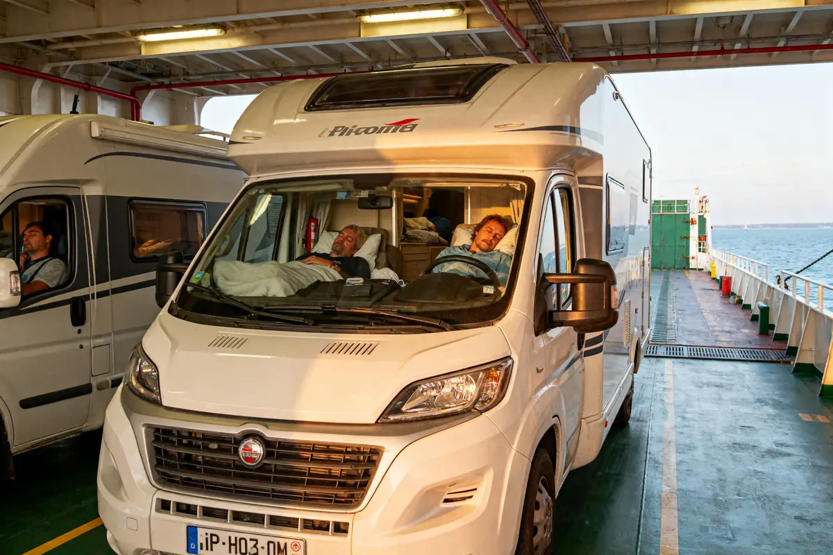 Camping-cars sur un ferry, deux personnes endormies à l'intérieur du véhicule, en mer par temps agréable.