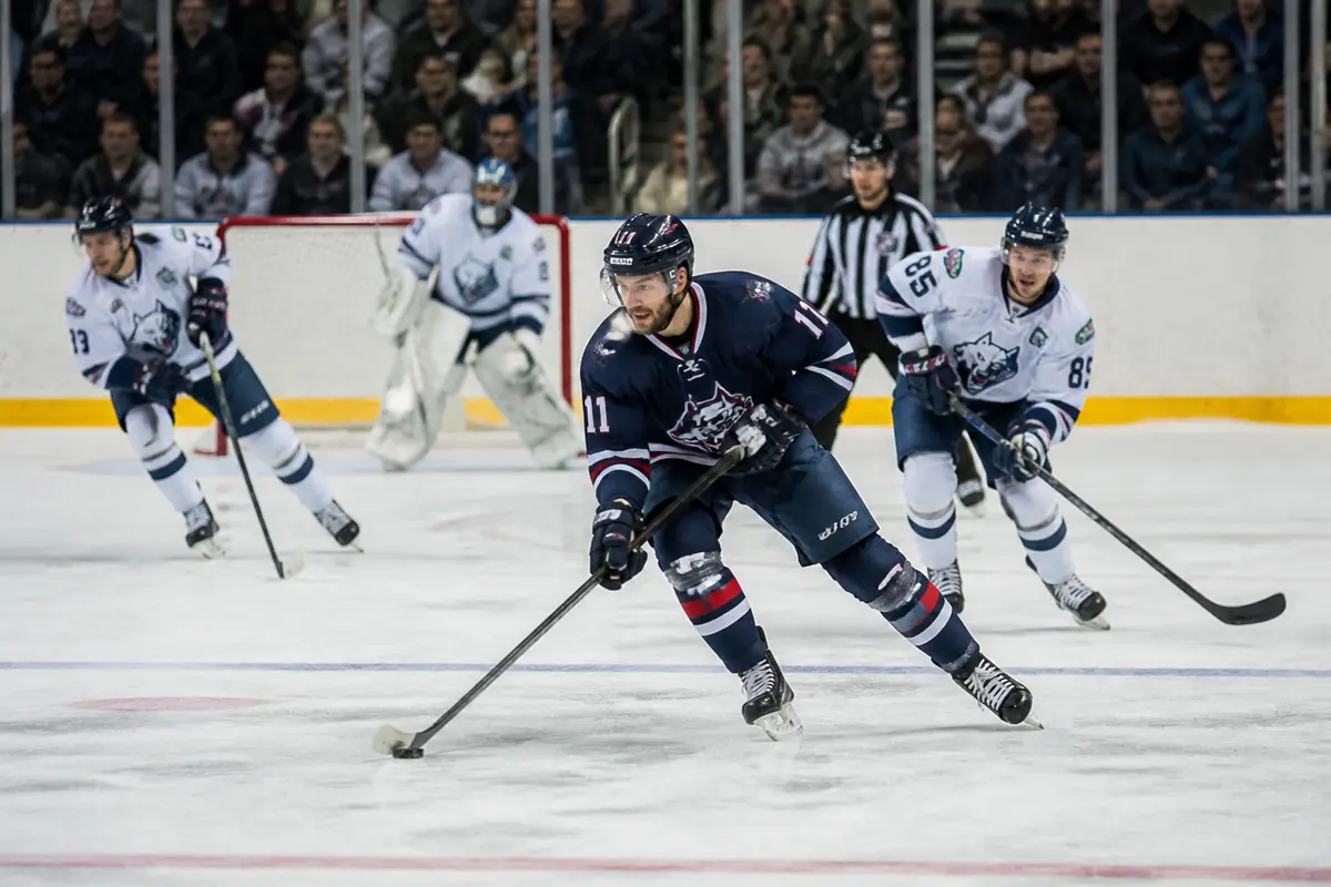 Joueurs de hockey sur glace en action sur la patinoire avec public en arrière-plan.