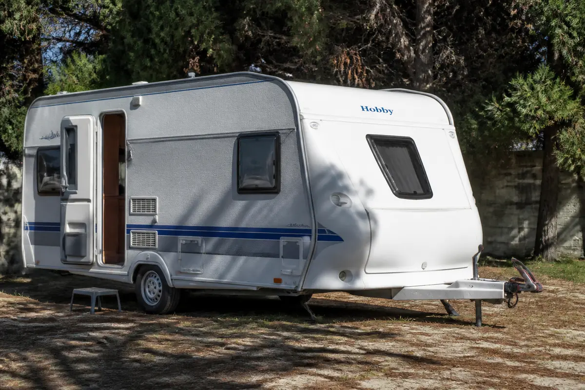 Caravane Hobby blanche stationnée dans un jardin ombragé avec porte entrouverte