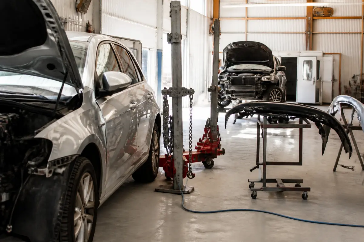 Atelier de réparation automobile avec capots ouverts et pare-chocs démontés, équipement de levage visible.
