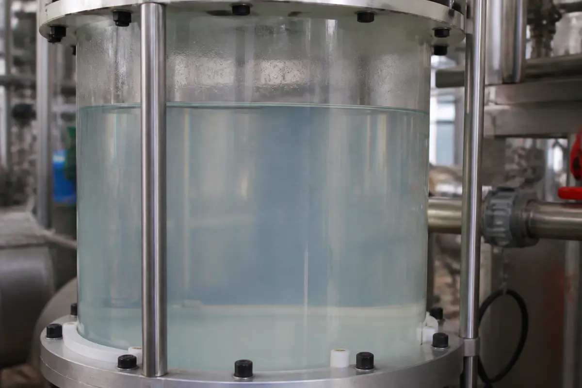 Gros plan sur un réservoir cylindrique en métal contenant un liquide clair dans une installation industrielle.