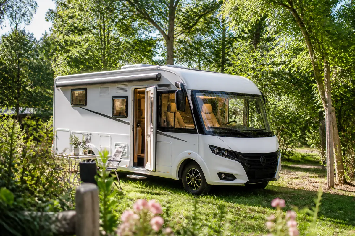 Camping-car stationné dans un cadre verdoyant, entouré d'arbres et de végétation.