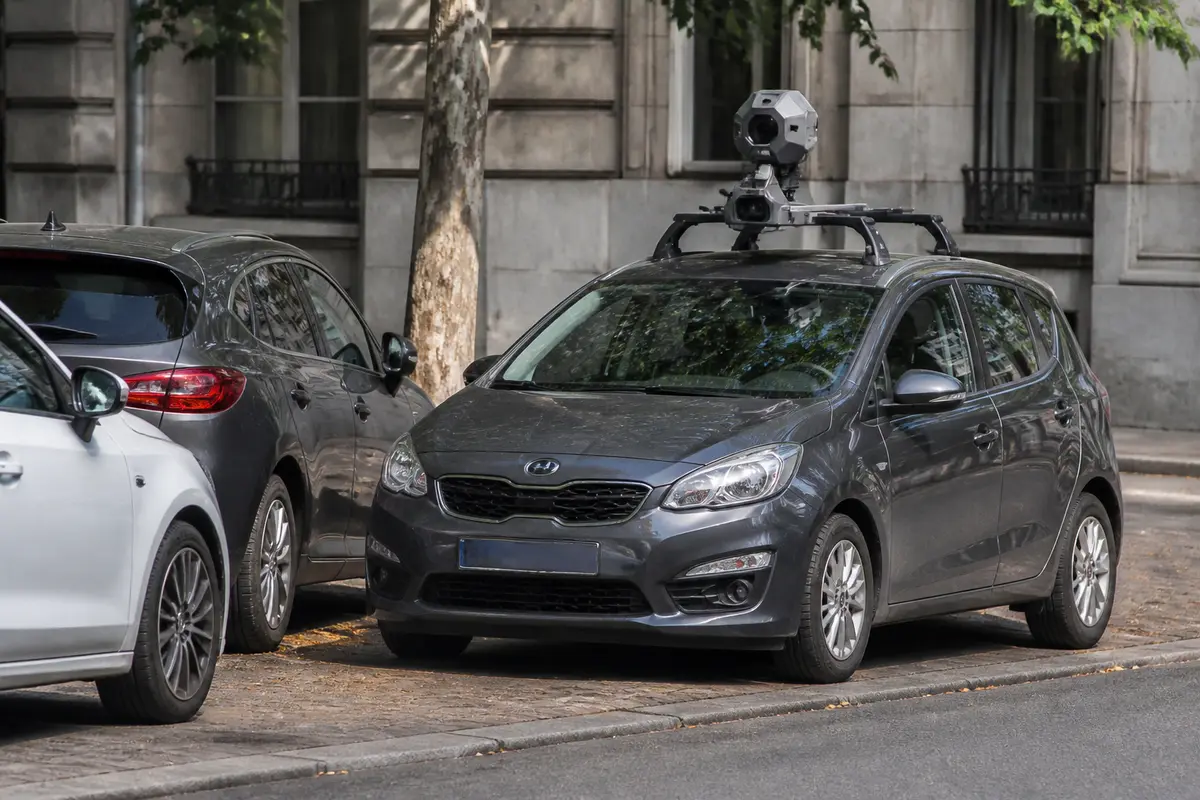 Voiture équipée d'une caméra sur le toit, stationnée sur trottoir, à côté d'autres véhicules urbains.