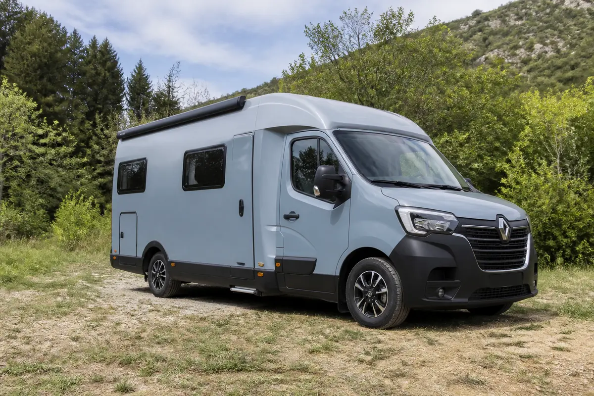 Camping-car Renault gris stationné dans un cadre naturel verdoyant, ciel clair en arrière-plan.